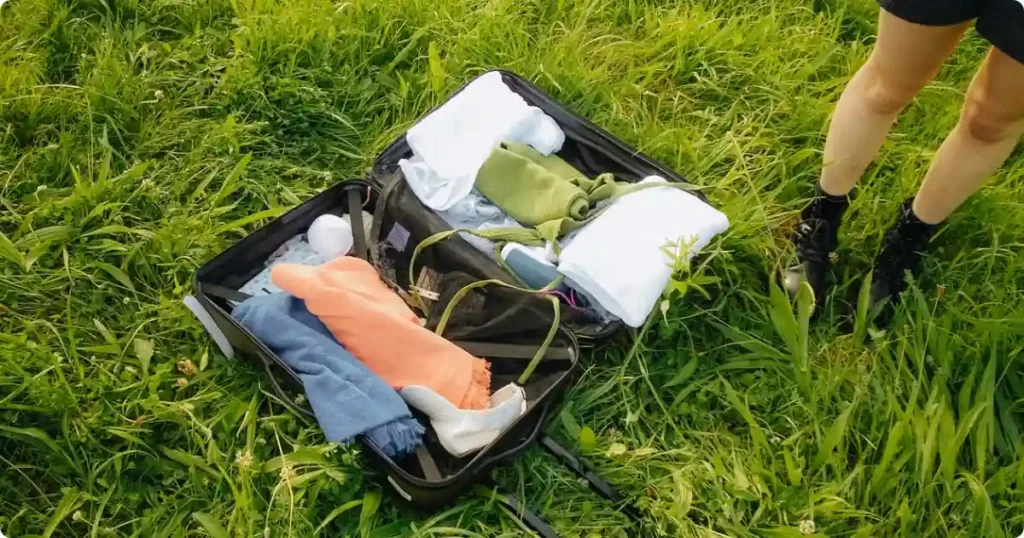 Beach gear essentials including tote bag, towel, sunscreen, and water bottle arranged on sandy beach