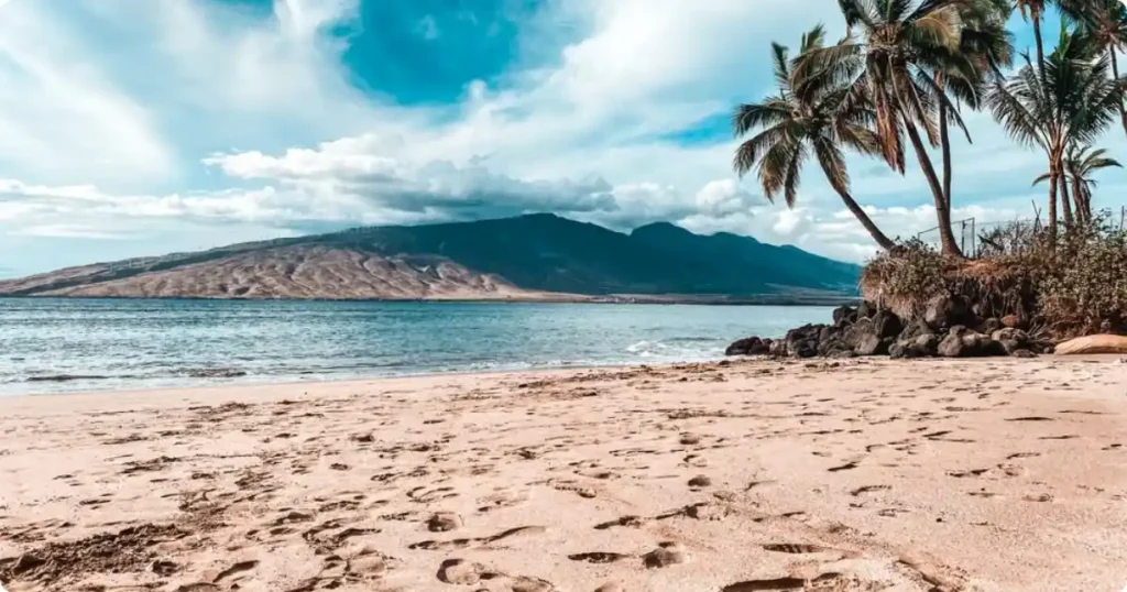 Golden sand beach in Maui Hawaii with clear turquoise ocean water and volcanic coastline